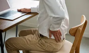 Homme assis à un bureau, se tenant le bas du dos. Il se demande combien de temps d'arrêt pour une discopathie.