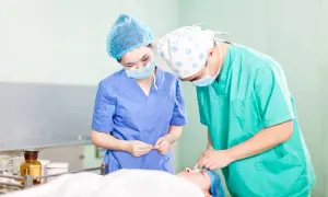 Deux chirurgiens masqués et coiffés préparent une intervention. L'un tient des instruments, l'autre s'occupe du patient. Ils se demandent "que veut dire DAE" dans ce contexte médical.