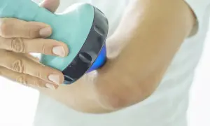 Une main utilise un appareil bleu clair pour soigner une tendinite au coude. La lumière bleue émise par l'appareil cible la zone douloureuse.