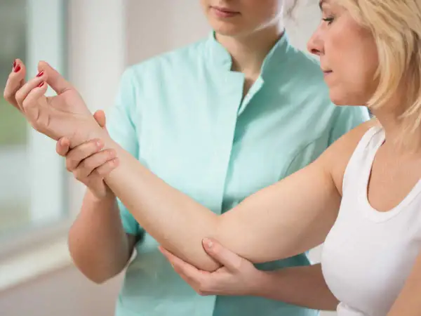 Une thérapeute examine le bras d'une patiente, possiblement pour une nevralgie cervico brachiale.