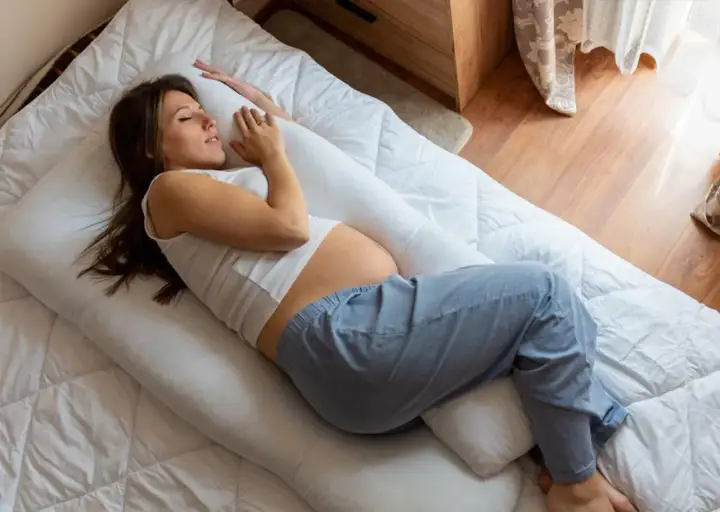Une femme enceinte, en plein début de grossesse, peine à trouver le sommeil malgré un coussin de maternité.